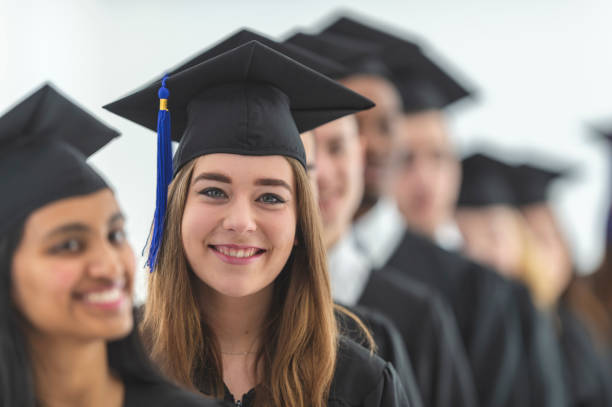 A young woman is smiling as she stands among her graduating class at their ceremony.